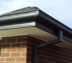 Residential roof with gutters and downpipe installed on a brick home
