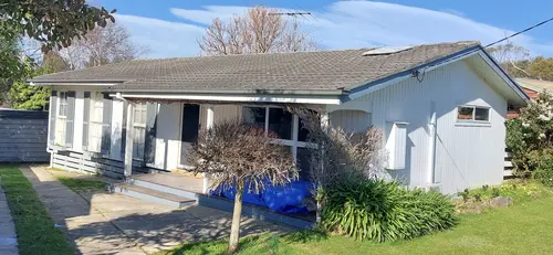 Single-story suburban house with dark gray shingled roof, tall windows with shutters, and small porch.